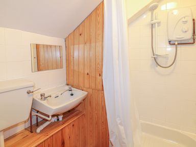 A small bathroom with a sink toilet shower and wooden panels at The Wagon Linney in Bude