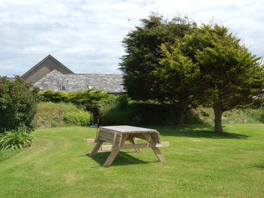 A wooden picnic table on a grass lawn with trees and a building in the background at The Wagon Linney in Bude