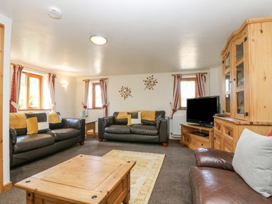 A living room with two black sofas a brown armchair a wooden coffee table a television and wooden furniture at The Wagon Linney in Bude