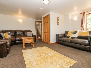 A living room with two leather sofas a wooden coffee table a yellow patterned rug and wooden doors at The Wagon Linney in Bude