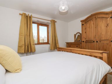 A bedroom with a wooden bed frame a wooden wardrobe a wooden dresser with a mirror and yellow curtains at The Wagon Linney in Bude