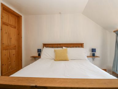 A bedroom with a wooden bed frame a white bedspread a yellow pillow two blue lamps and a wooden door at The Wagon Linney in Bude