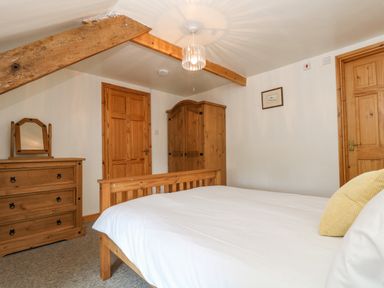 A bedroom with wooden bed frame white bedding wooden wardrobe and chest of drawers at The Wagon Linney in Bude