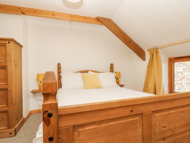 A bedroom with a wooden bed a yellow pillow and lamps a wooden wardrobe and a window with yellow curtains at The Wagon Linney in Bude