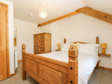 A bedroom with a wooden bed with white bedding two bedside tables with yellow lamps and a wooden wardrobe at The Wagon Linney in Bude