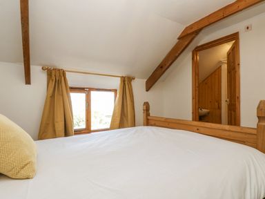 A bedroom with a wooden bed frame white bedding a yellow pillow and a window with curtains at The Wagon Linney in Bude