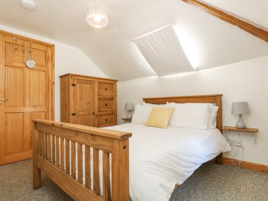 A bedroom with a wooden bed frame white bedding and a yellow pillow a wooden wardrobe a wooden door and bedside tables with lamps at The Wagon Linney in Bude