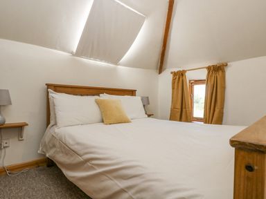 A bedroom with a bed with white bedding and a yellow cushion a window with curtains and a skylight at The Wagon Linney in Bude