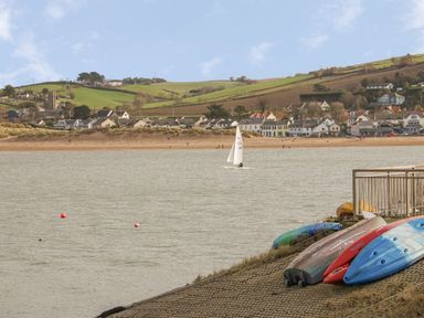 A river with a sailboat and kayaks on the shore with houses and green hills in the background at Devonair in Westward Ho