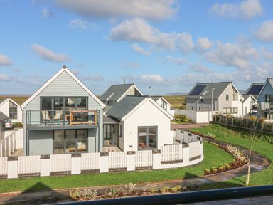 A modern house with a balcony and fenced garden surrounded by grass and a pathway at Devonair in Westward Ho