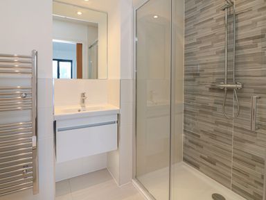 A bathroom with a sink and mirror a glass shower enclosure and a towel radiator at Devonair in Westward Ho