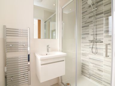 A bathroom with a wall-mounted sink, a chrome towel radiator, and a glass-enclosed shower at Devonair in Westward Ho