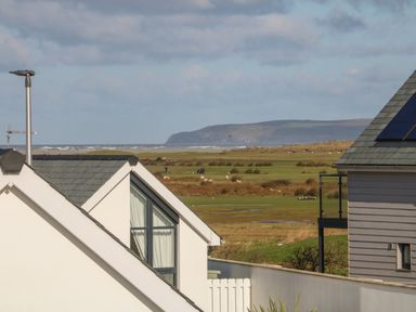 A view of rooftops overlooking a grassy field with sheep and hills in the distance at Devonair in Westward Ho