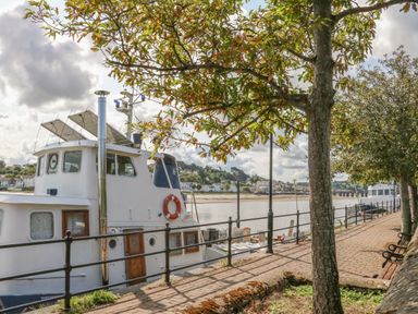 A walkway along a river with trees benches and boats docked at Devonair in Westward Ho