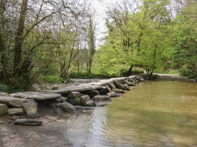 A stone stepping bridge crossing a shallow river with surrounding trees at Devonair in Westward Ho