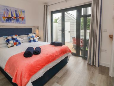 A bedroom with a bed with patterned pillows and folded towels by glass doors leading to a patio at Devonair in Westward Ho