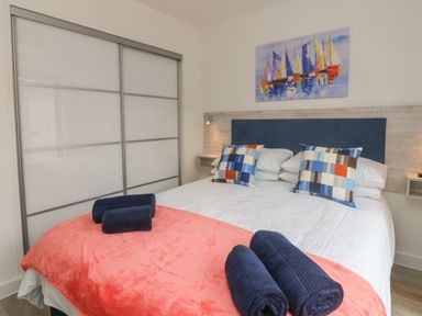 A bedroom with a bed with white bedding and colorful pillows navy towels on a coral blanket and a painting above the bed at Devonair in Westward Ho