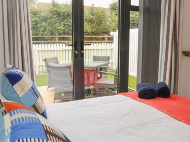 A bedroom with bed and pillows facing glass doors showing outdoor table and chairs at Devonair in Westward Ho