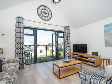 A living room with a sofa coffee table and television by glass doors opening to a balcony at Devonair in Westward Ho