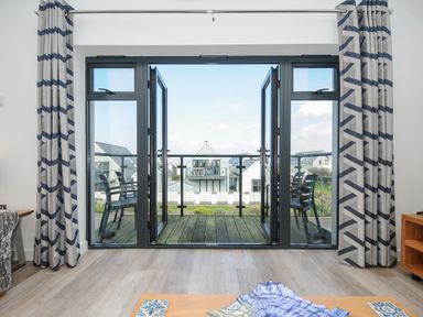 A room with open double glass doors leading to a balcony with chairs and houses visible outside at Devonair in Westward Ho