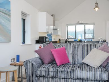 A striped sofa with colorful cushions in a living area with a small side table and a kitchen in the background at Devonair in Westward Ho