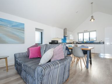 An open living room and kitchen with a striped sofa with cushions and a dining table with chairs at Devonair in Westward Ho