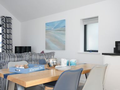 A dining table with cups plates and a teapot near a striped sofa and a painting at Devonair in Westward Ho
