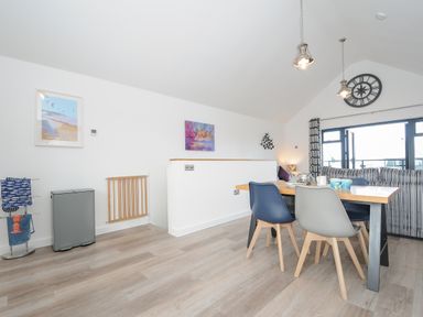 A dining area with a wooden table and mixed chairs next to a striped sofa and large windows at Devonair in Westward Ho