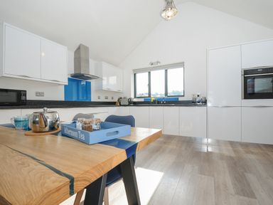 A kitchen with white cabinets a wooden table with a blue tray and kettle and a window above the sink at Devonair in Westward Ho