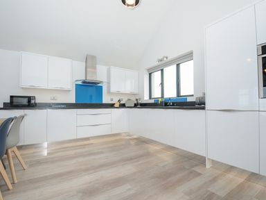 A kitchen with white cabinets black countertops blue glass splashbacks and wooden flooring at Devonair in Westward Ho