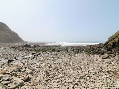 A rocky beach with stones and cliffs on both sides and waves in the background at The Stable in Bude