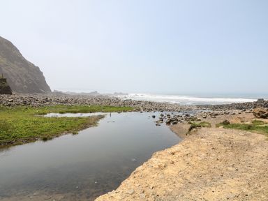 A rocky coastal area with a small water body and grassy patches near the sea at The Stable in Bude