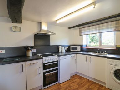 A kitchen with white cabinets, stove, dishwasher, microwave, sink, and window at The Stable in Bude
