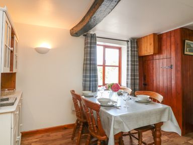 A dining table set with bowls glasses and cutlery near a window with curtains in a room with wooden paneling and white walls at The Stable in Bude