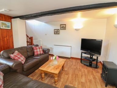 A living room with brown leather sofas a wooden coffee table with a vase of flowers a television on a glass stand and framed pictures on the wall at The Stable in Bude