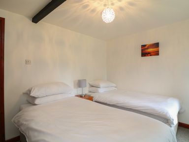 A bedroom with two single beds with white bedding a nightstand with a lamp and a wall picture at The Stable in Bude