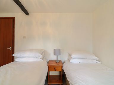 A bedroom with two single beds white bedding a wooden nightstand with a lamp between the beds and a wooden door in the corner at The Stable in Bude