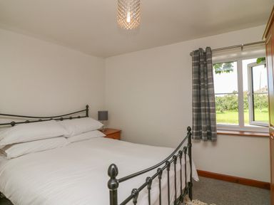 A bedroom with a metal bed frame a wooden nightstand with a lamp a window with plaid curtains and a wardrobe at The Stable in Bude