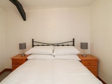 A bedroom with a bed with white bedding flanked by wooden nightstands with lamps at The Stable in Bude