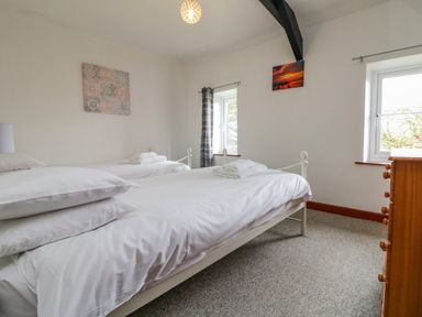 A bedroom with two single beds with white bedding two windows and a wooden dresser at The Stable in Bude
