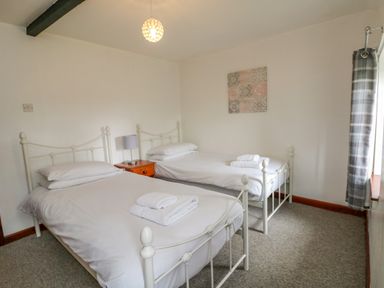 A bedroom with two single beds a wooden nightstand with a lamp between the beds and a window with plaid curtains at The Stable in Bude