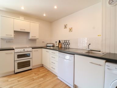 A kitchen with white cabinets black countertops a stove sink dishwasher and washing machine at The Dairy in Bude