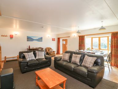 A living room with black leather sofas and a wooden coffee table next to a dining table by a window at The Dairy in Bude
