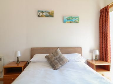 A bedroom with a bed a pillow two bedside tables with lamps and two paintings on the wall at The Dairy in Bude