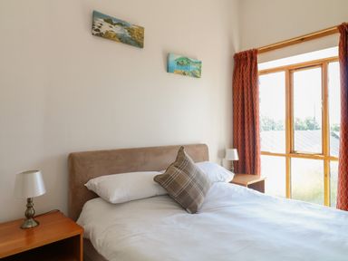A bedroom with a bed pillows bedside tables lamps paintings and a window with orange curtains at The Dairy in Bude