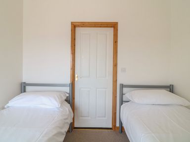 A bedroom with two single beds and a white door in the middle at The Dairy in Bude