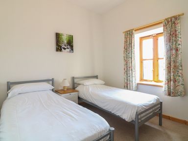A bedroom with two single beds a bedside table with a lamp a window with floral curtains and a nature picture on the wall at The Dairy in Bude