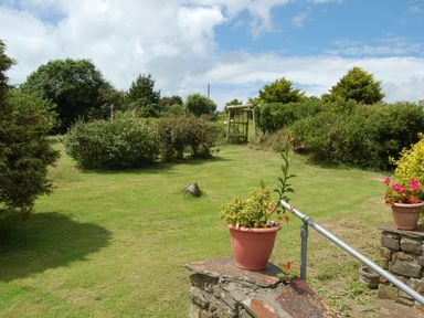 A garden with bushes trees a wooden swing and potted plants on stone walls at The Shippon in Bude