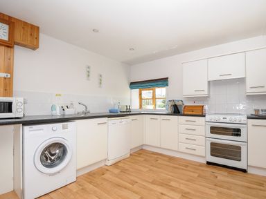A kitchen with white cabinets a washing machine dishwasher oven microwave and wooden floor at The Shippon in Bude