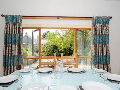 A dining table set with plates and glasses in front of a window with floral curtains at The Shippon in Bude